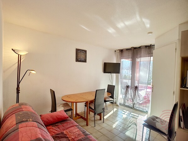 A room with a bed, a table, chairs, a TV, and a window with curtains. - 1BR Flat with terrace, parking and wifi in Lamalou (Lamalou-les-Bains)