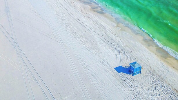 En strand med krystalklart turkis vand, en sandet kystlinje og nogle få strandparasoller.