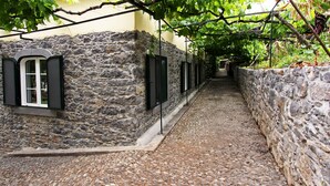A narrow cobblestone alleyway with stone walls and black shutters on windows. - Casa das Vinhas (Funchal)