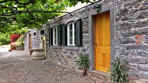 A stone building with a wooden door and three arched windows with shutters. - Casa das Vinhas (Funchal)