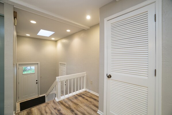 A hallway with a white door, a white railing, and a wooden floor.