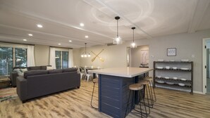 Una sala de estar moderna con un sofá gris, una isla de cocina con taburetes y un comedor con mesa y sillas blancas.