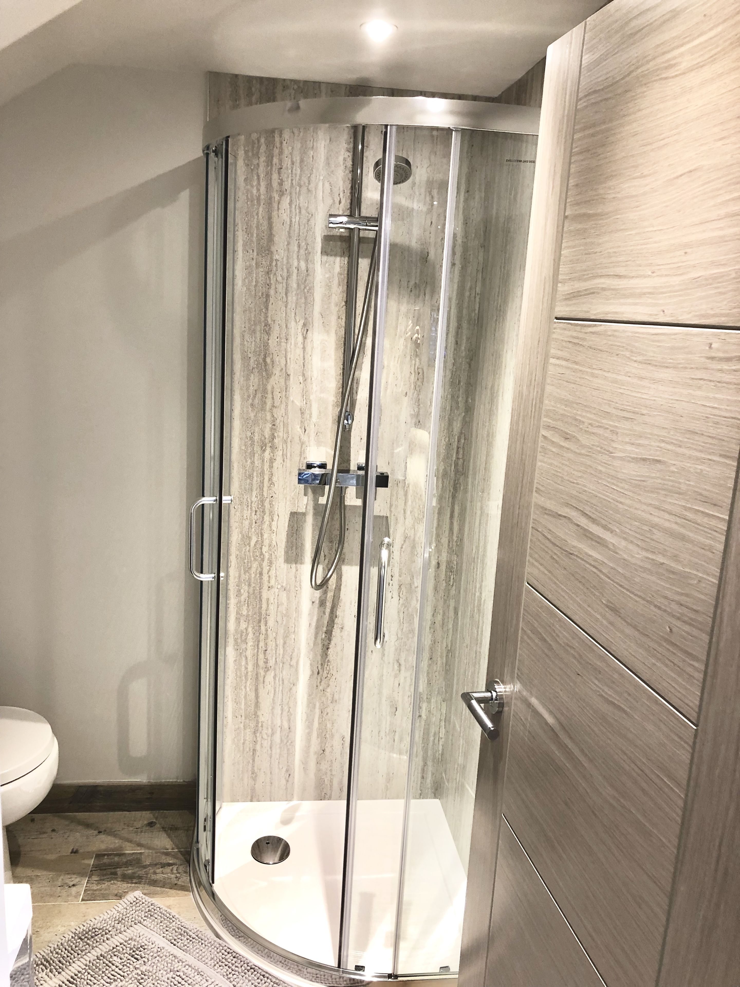 Une cabine de douche moderne dotée d’une porte en verre, d’un pommeau de douche et d’un flexible de douche.