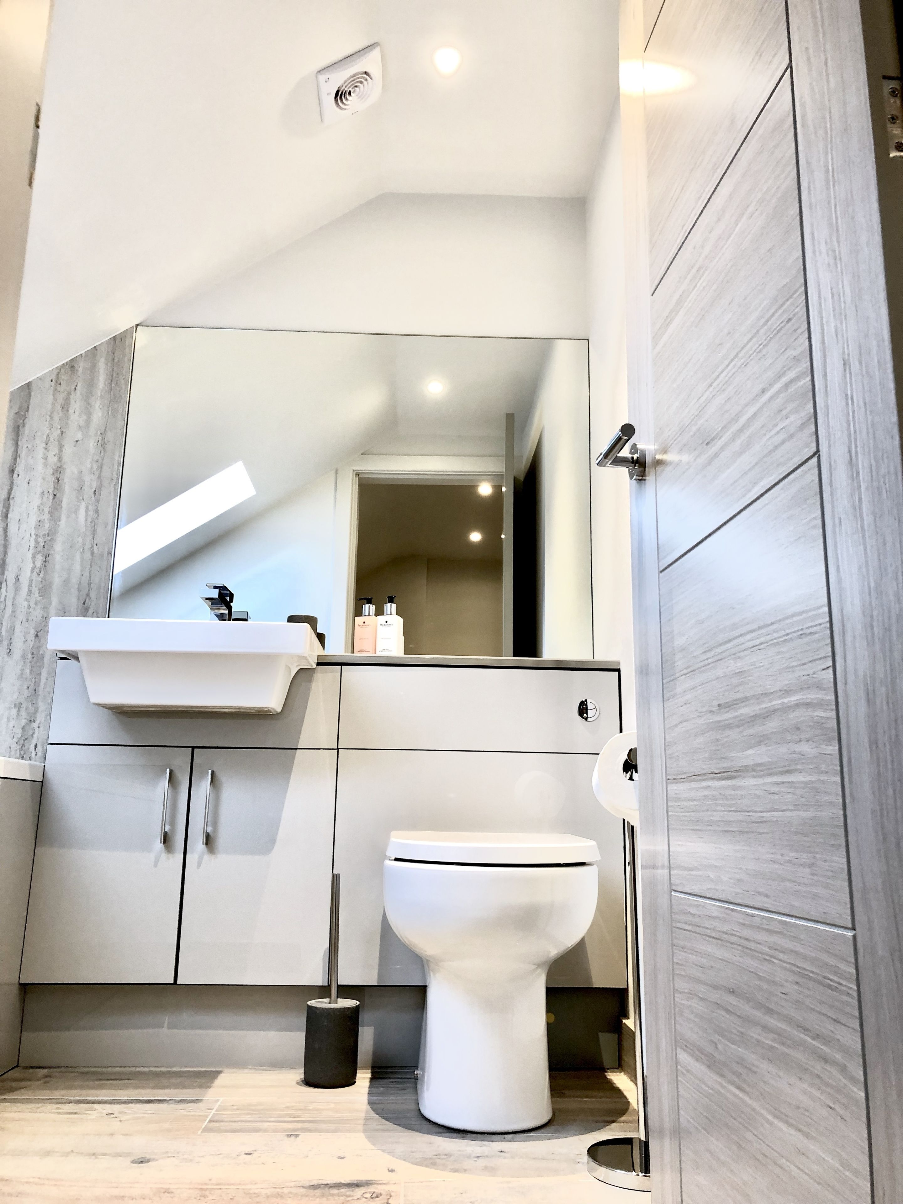 Un baño moderno con un lavabo blanco, espejo y retrete.
