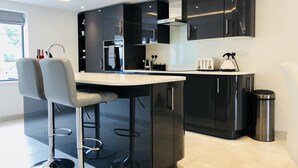 A modern kitchen with black cabinets, a stainless steel range hood, and a bar area with two bar stools. - Millstream Mews (Bakewell)