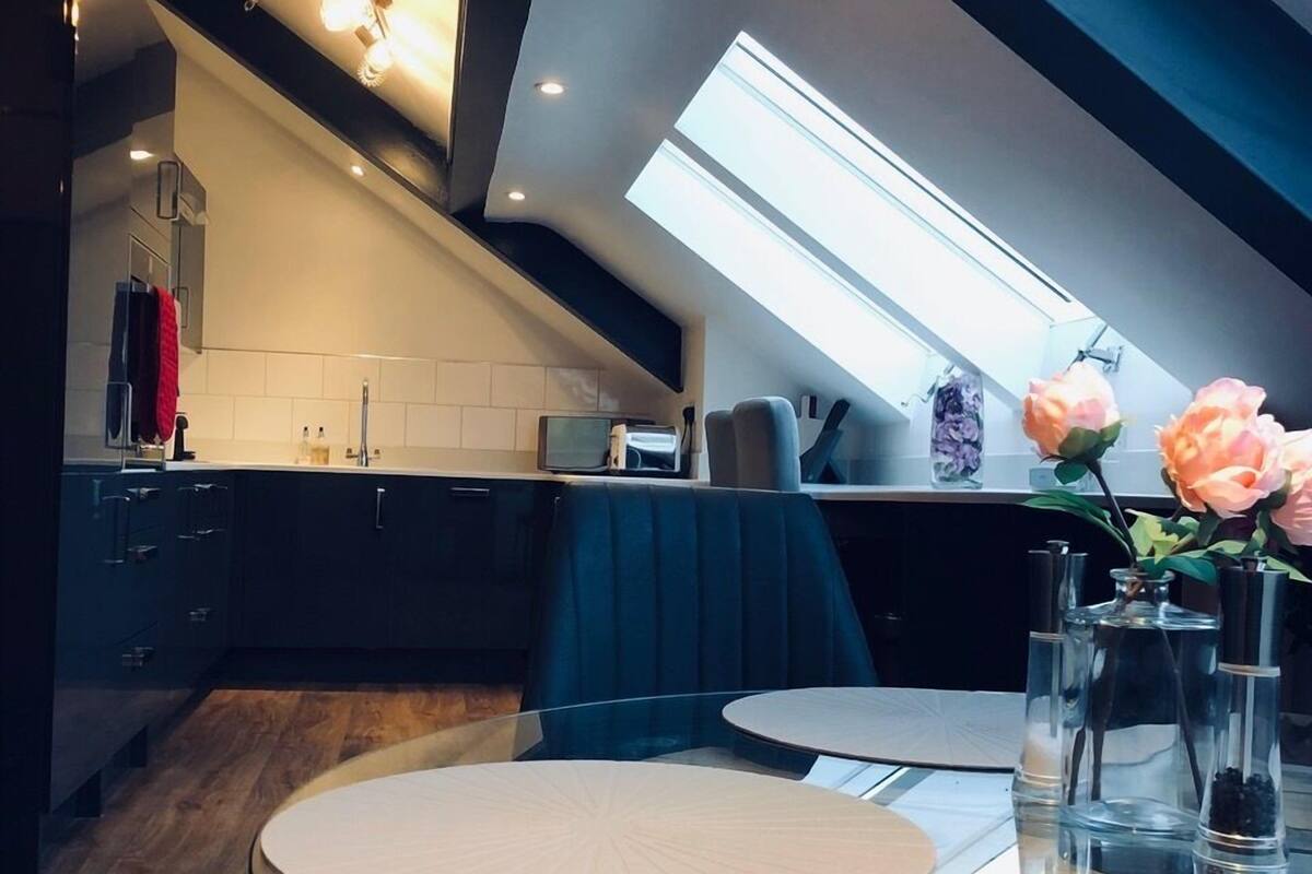 A modern kitchen with a skylight, dark cabinets, and a dining area with a glass table.