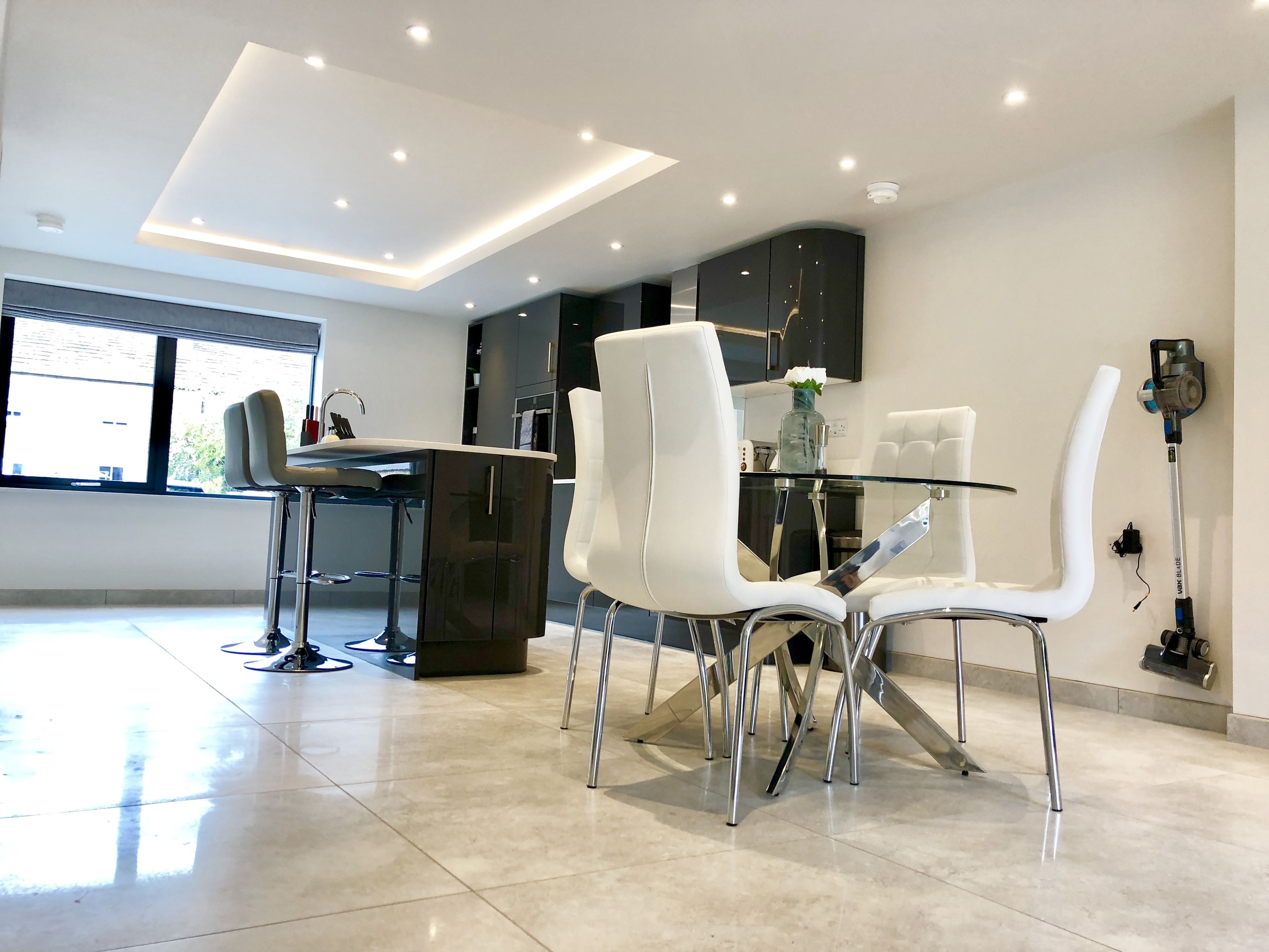A modern kitchen with a glass dining table, white chairs, and stainless steel appliances.