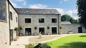 A stone building with multiple windows and doors, a paved courtyard, and a well-maintained lawn. - Millstream Mews (Bakewell)