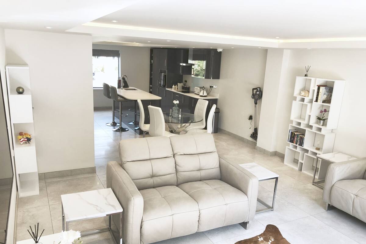 A modern living room with a sofa, a coffee table, and a cowhide rug. There is a dining area in the background with a table and chairs.