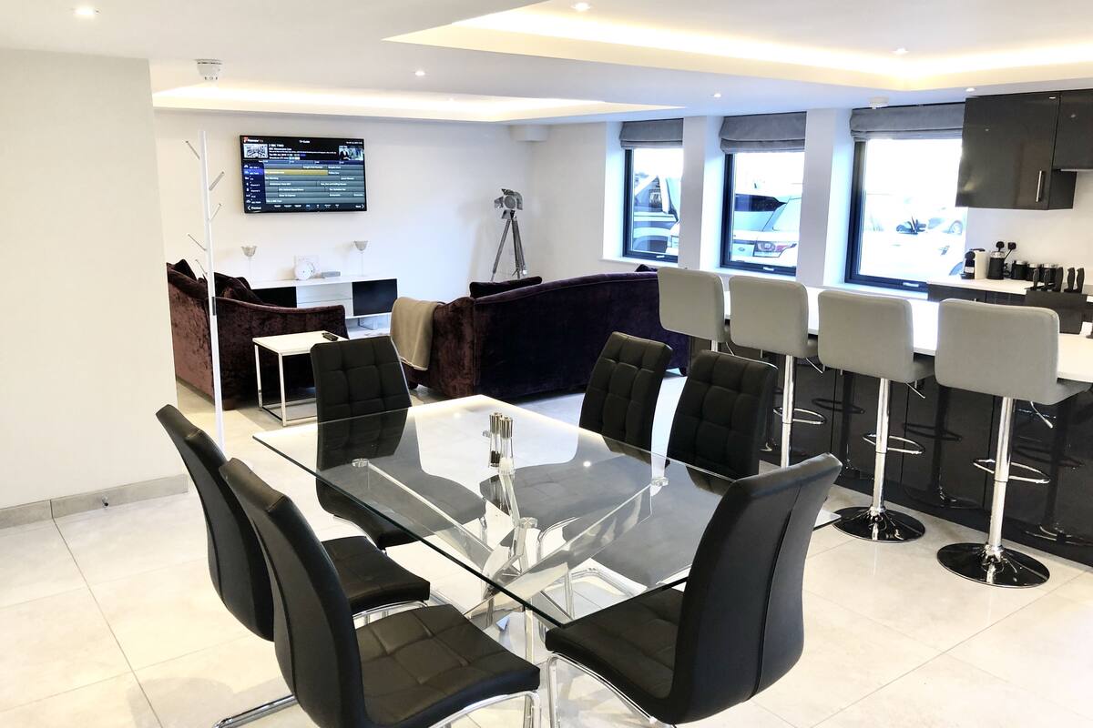 A modern meeting room with a glass table and black chairs, a sofa, and a TV displaying a program.