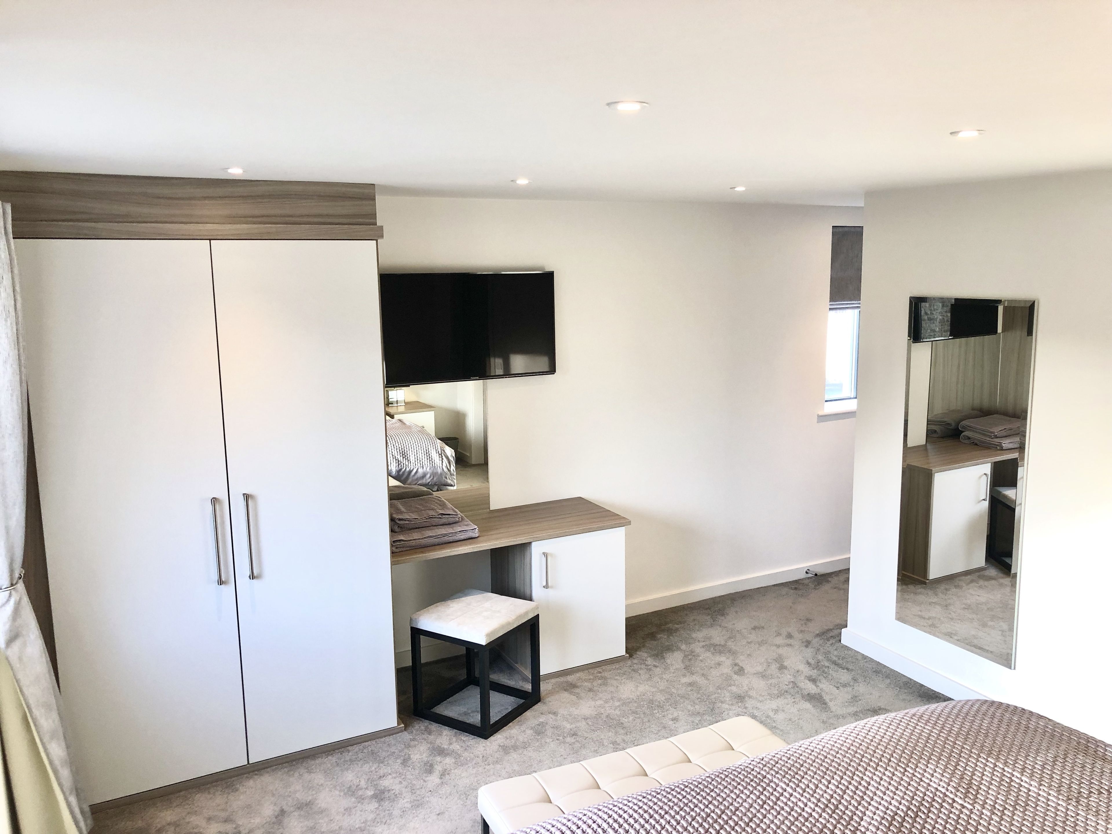 A modern bedroom with a large wardrobe, a flat-screen TV, a small table, and a bench.
