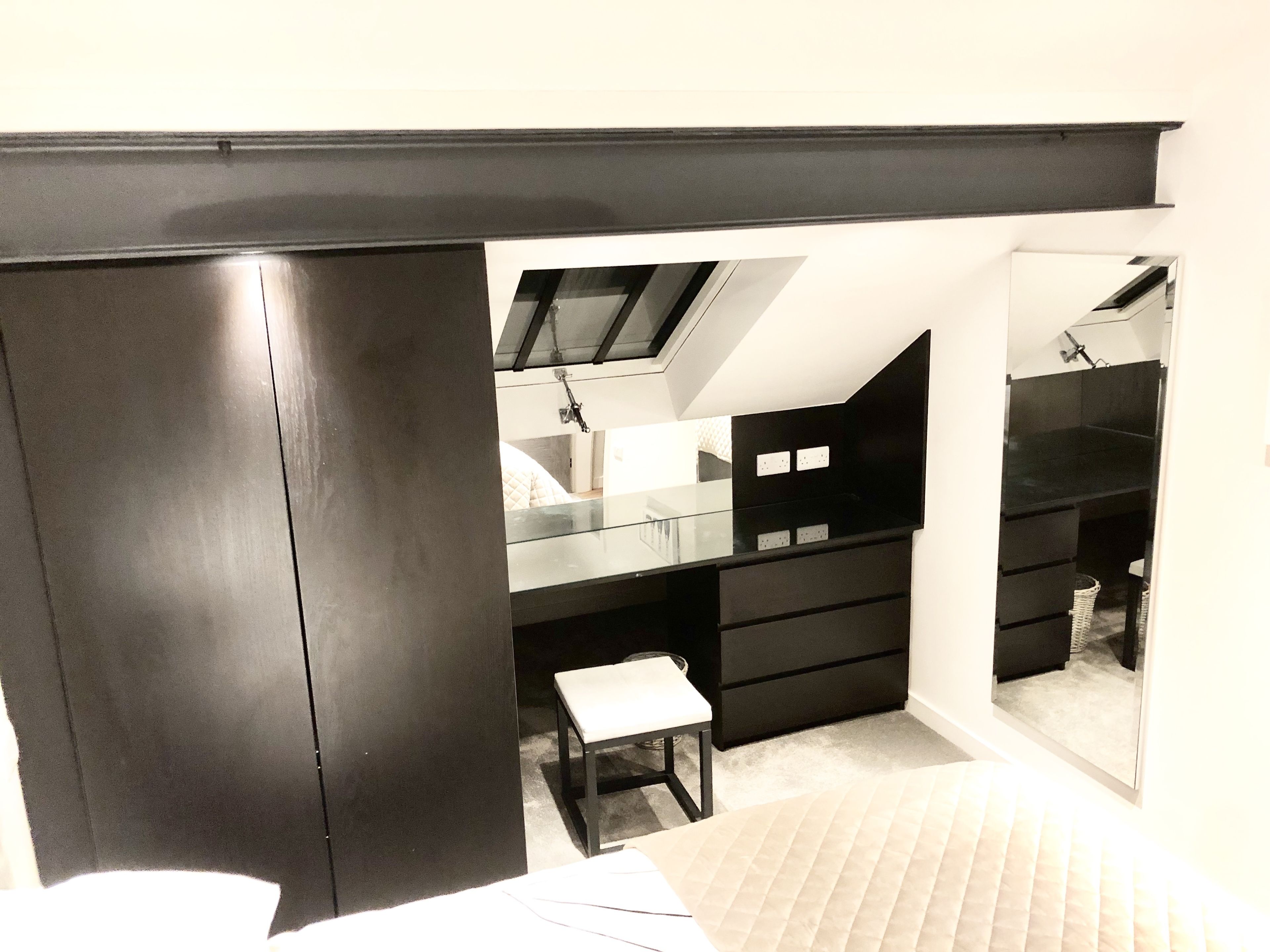 Un dormitorio con un armario grande, una cama, un taburete pequeño y un espejo.