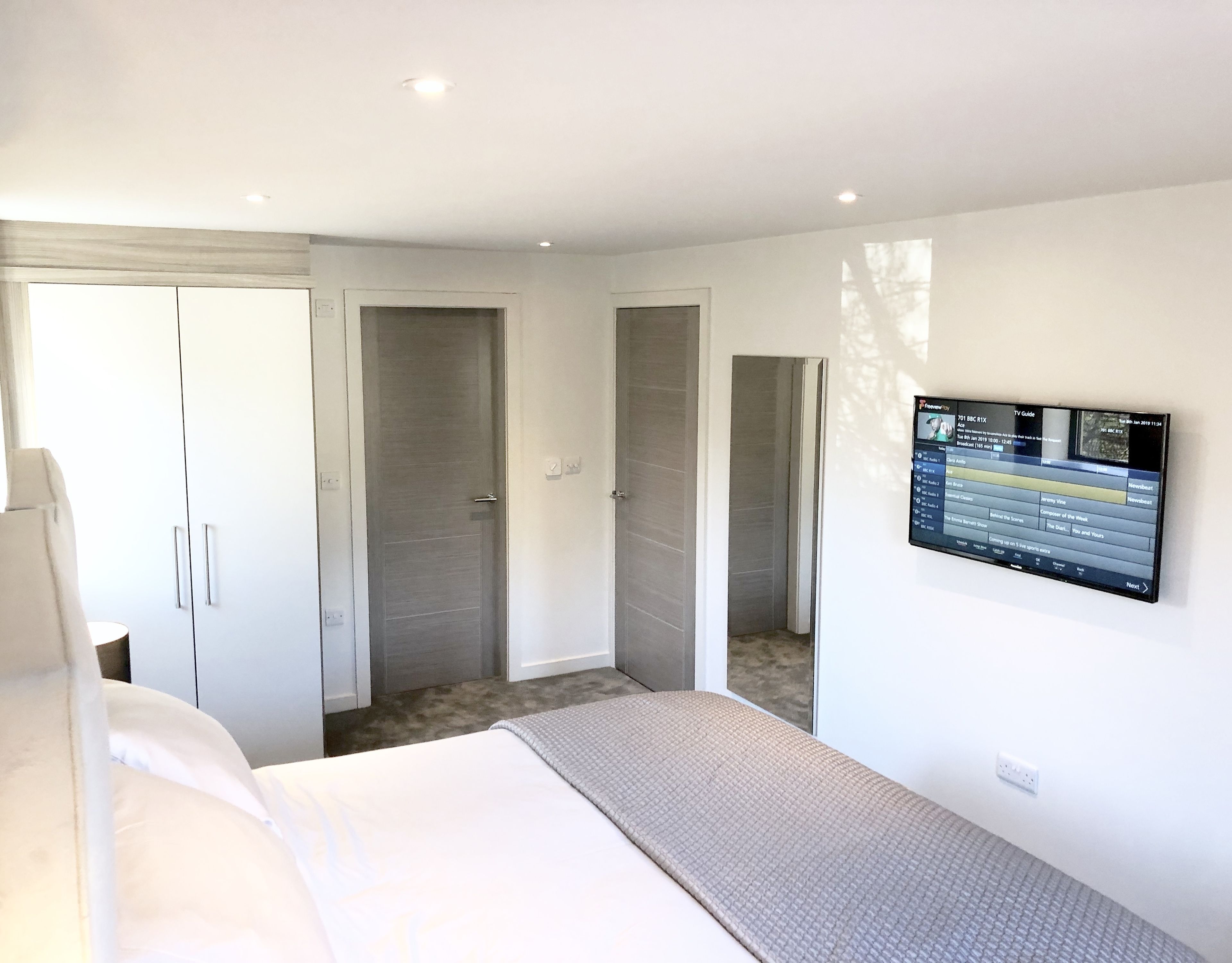 A modern hotel room with a bed, a TV mounted on the wall, and a wardrobe.