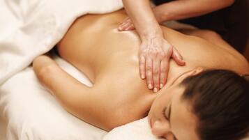 A person receiving a back massage on a bed with white linens.