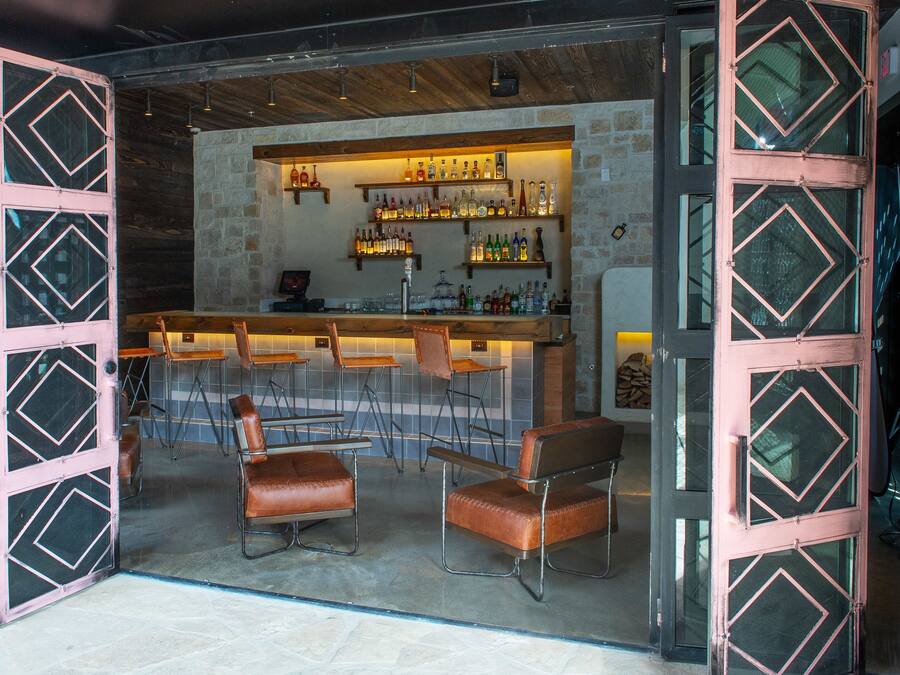 Un área de bar con pared de piedra, techo de madera y taburetes.