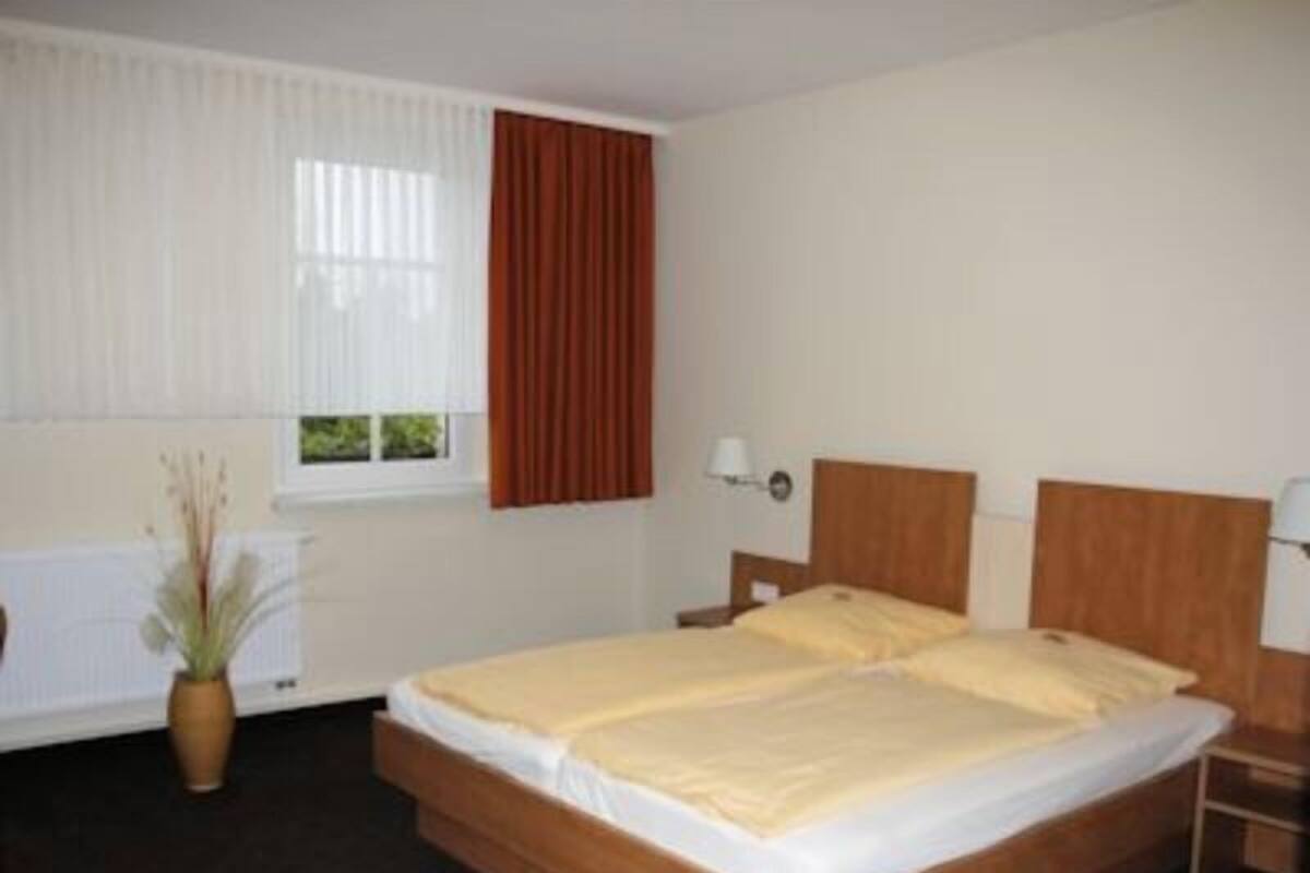 Une chambre d’hôtel avec un lit en bois, des rideaux blancs, une fenêtre avec des stores, une table de chevet et une lampe.