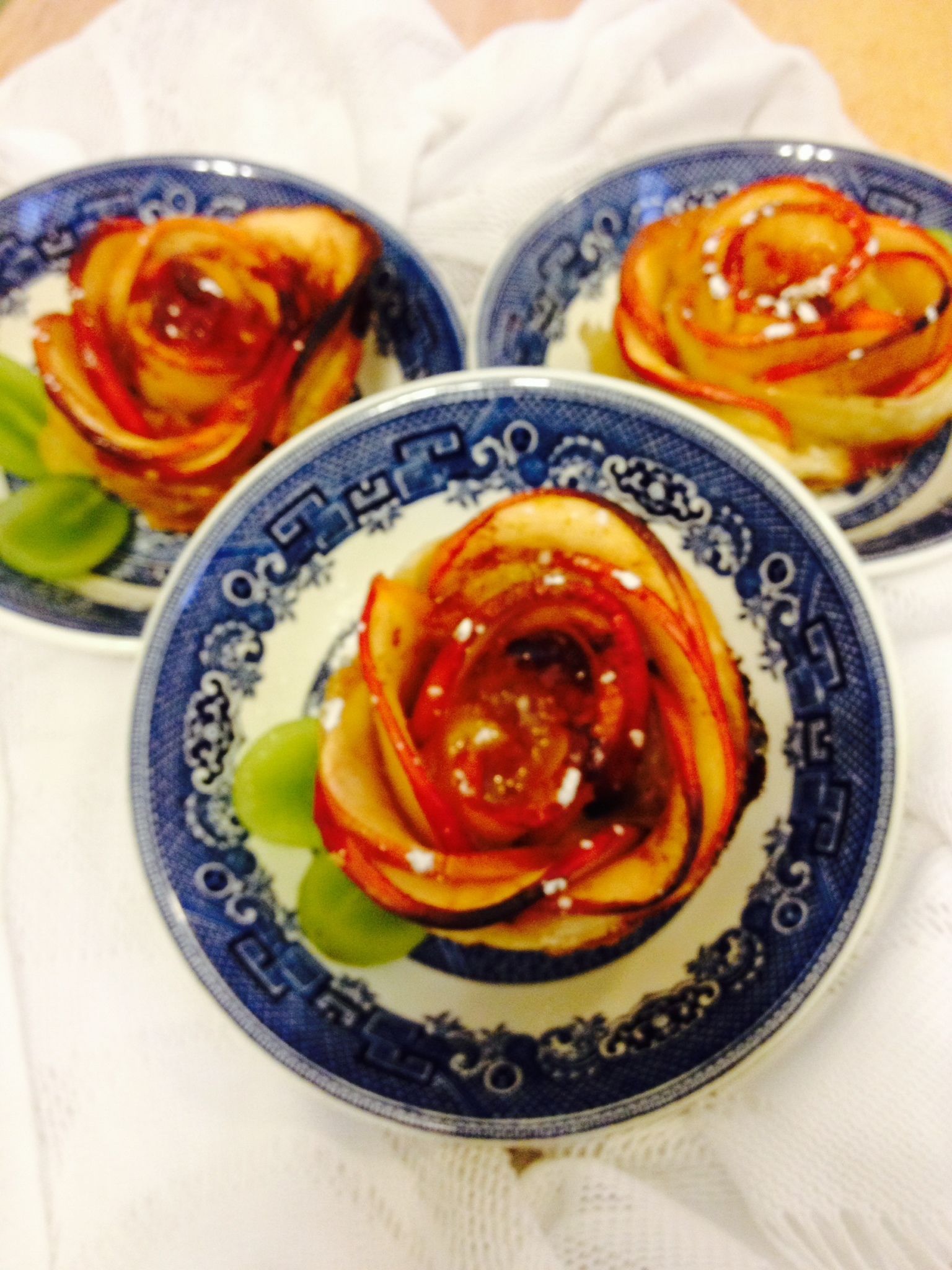 Three plates with a rose design, each containing slices of red fruit and green leaves.
