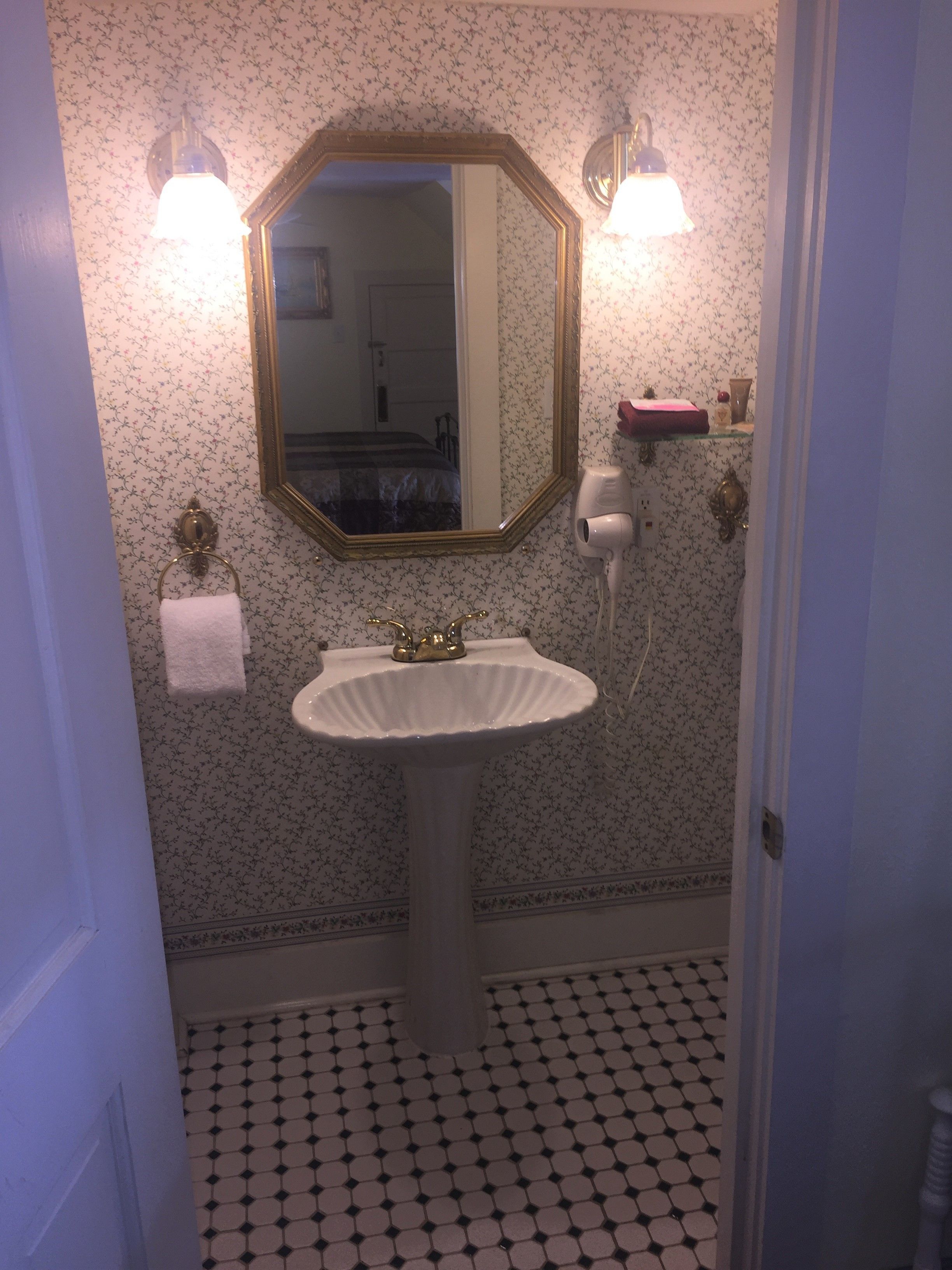 Un baño con lavamanos blanco, un espejo y un papel tapiz estampado.