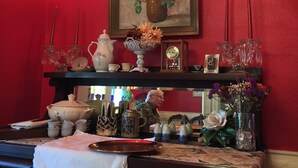 Una habitación con una pared roja, un cuadro de flores rojas y diversos objetos decorativos en estantes y mesas.