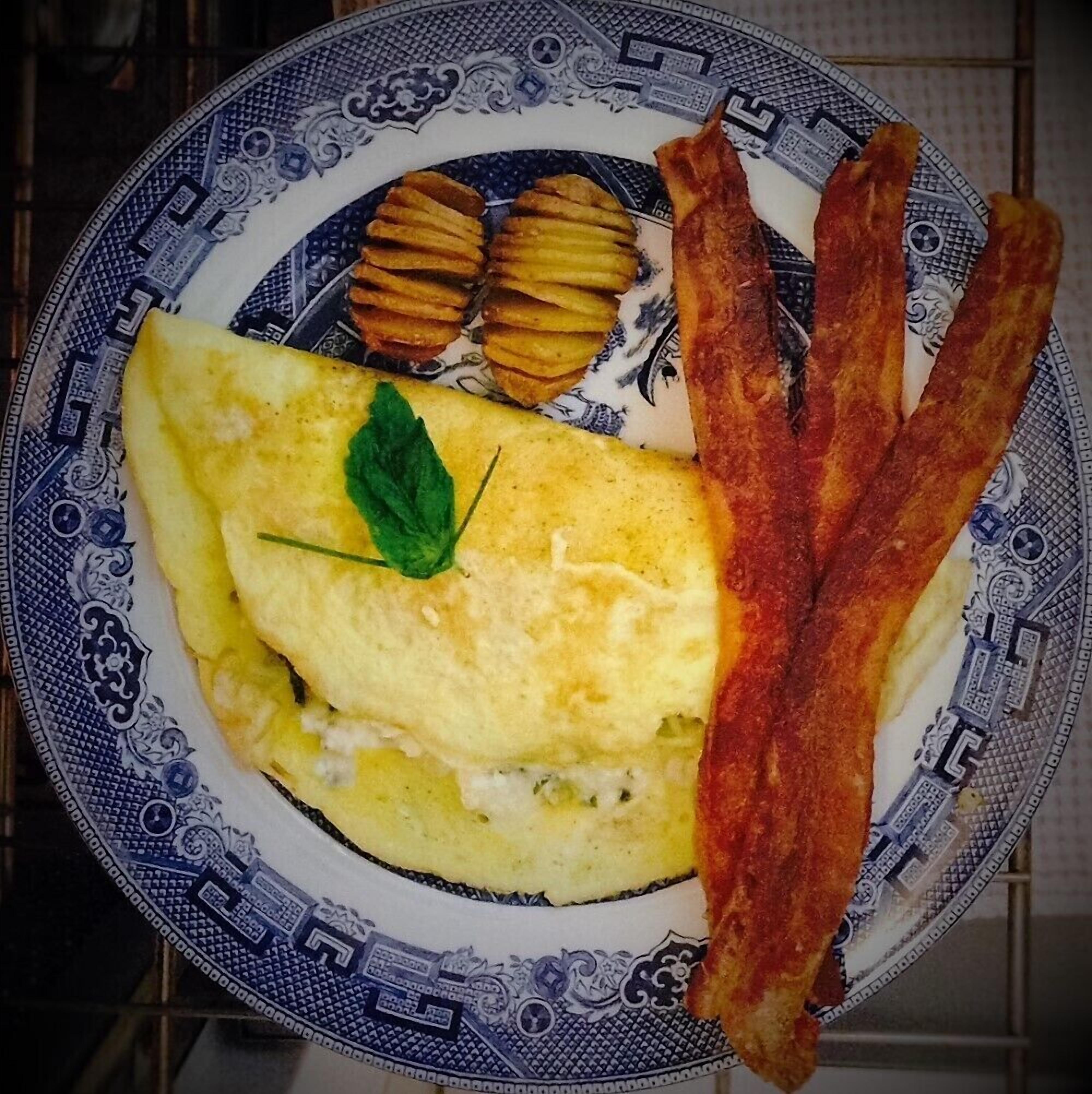 Een bord met een omelet, spek en gebakken aardappelen.