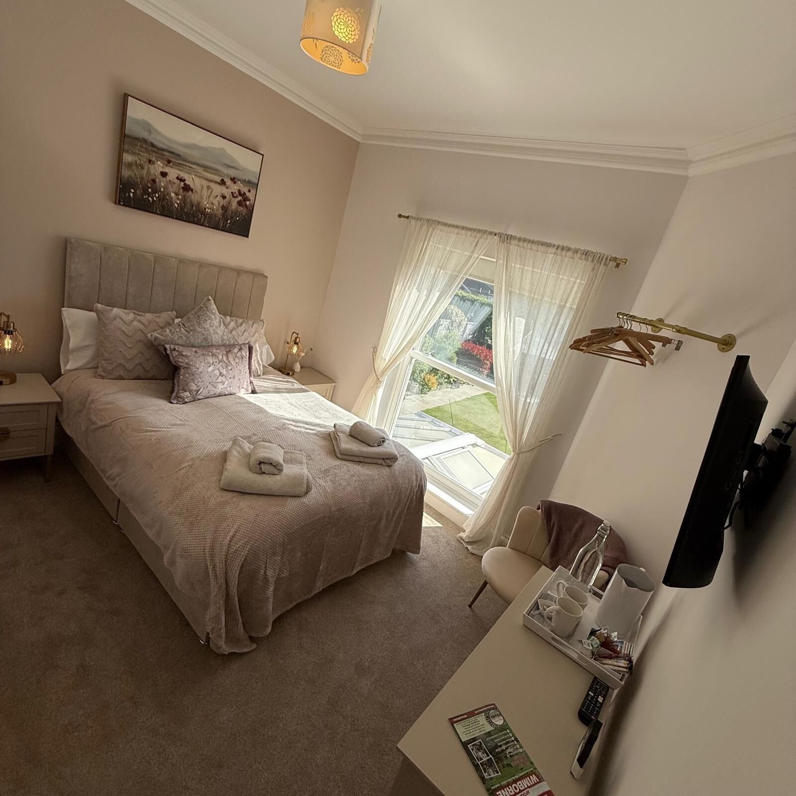 A bedroom with a bed, bedside tables, a window with curtains, a television, and a small table with a tray.