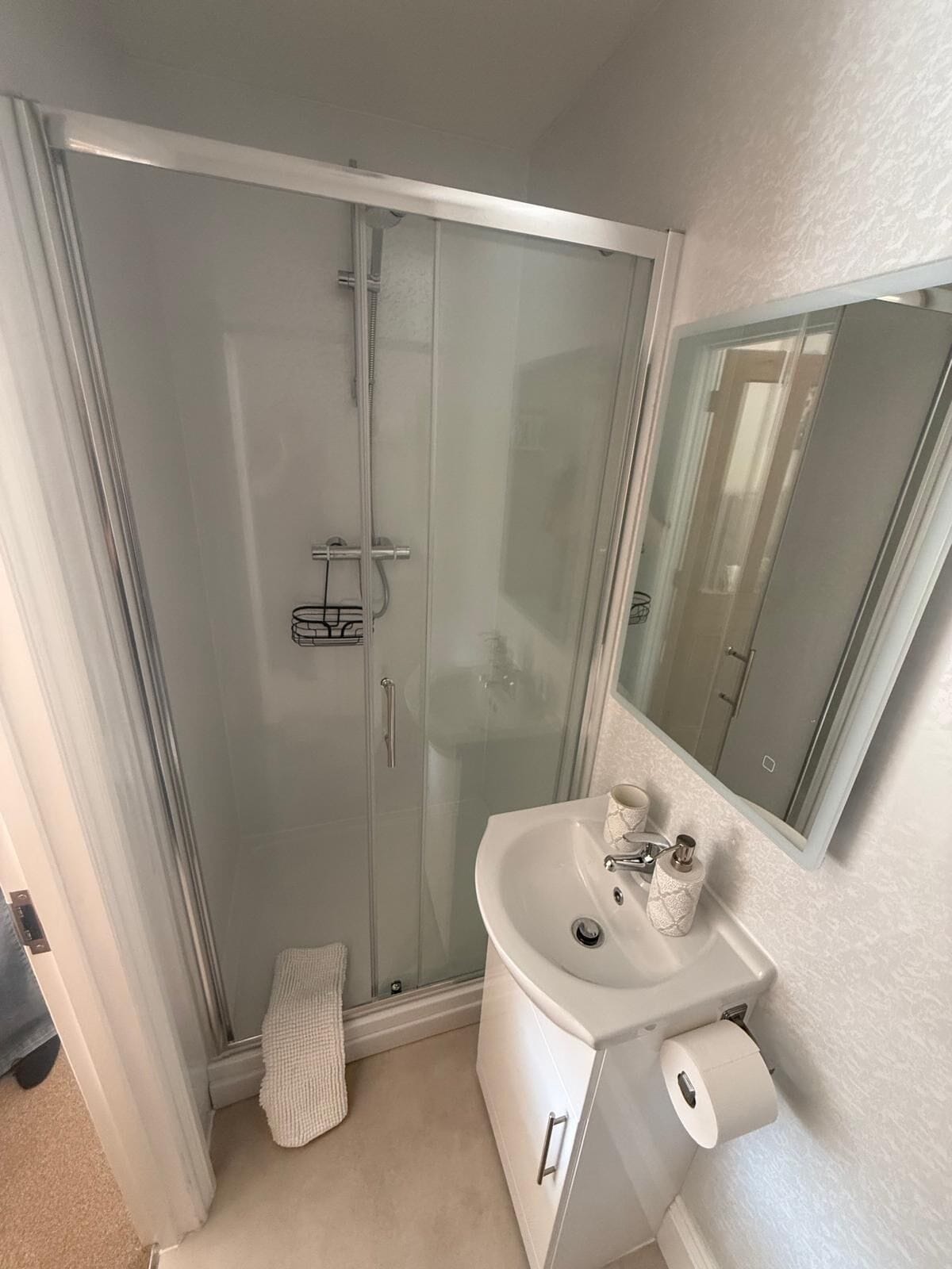 Een badkamer met een douche in een glazen cabine, een wit wastafelmeubel en een spiegel.