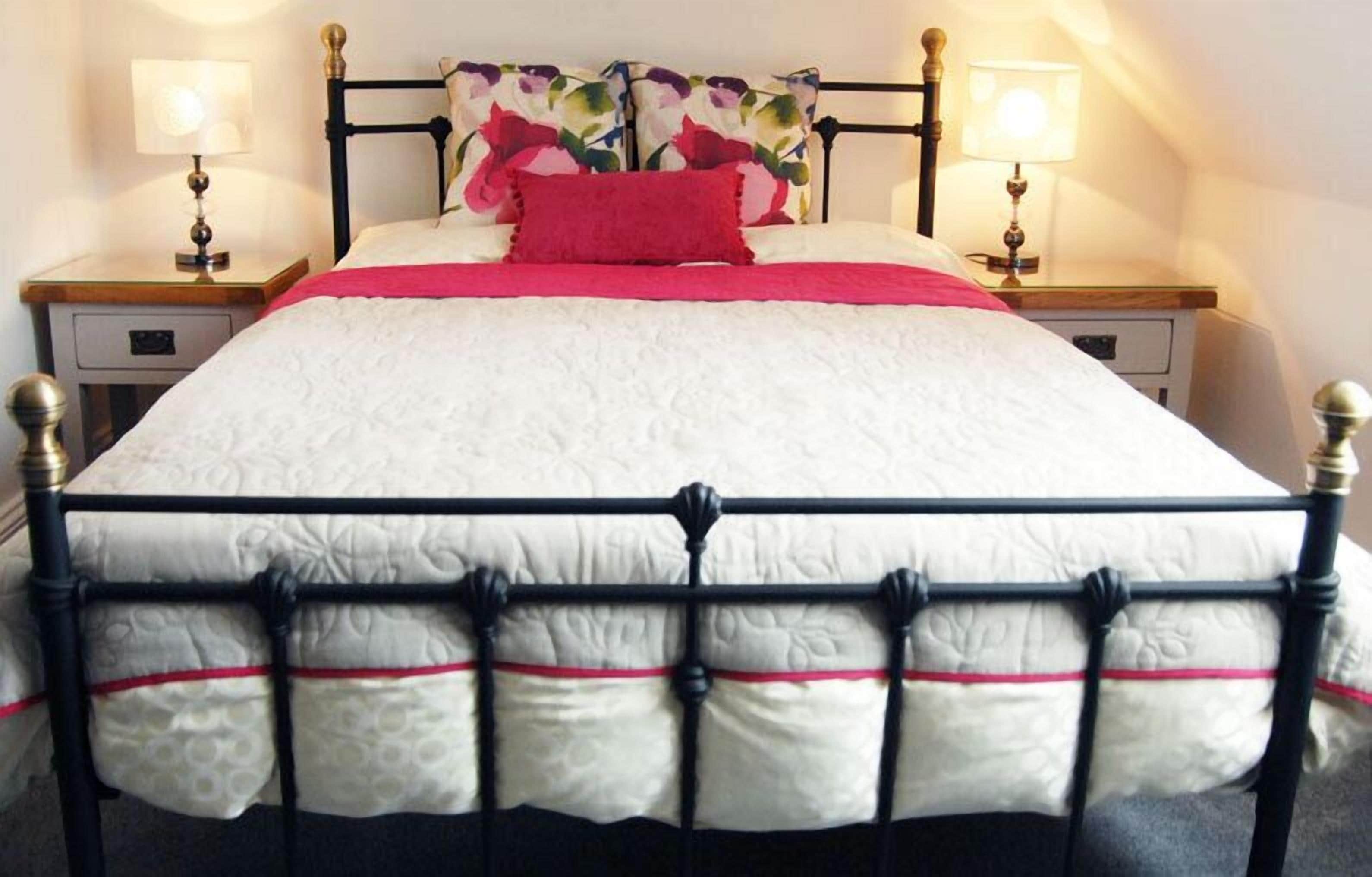 A bed with a white quilt, black metal frame, and red accents. There are two bedside tables with lamps and a floral headboard.