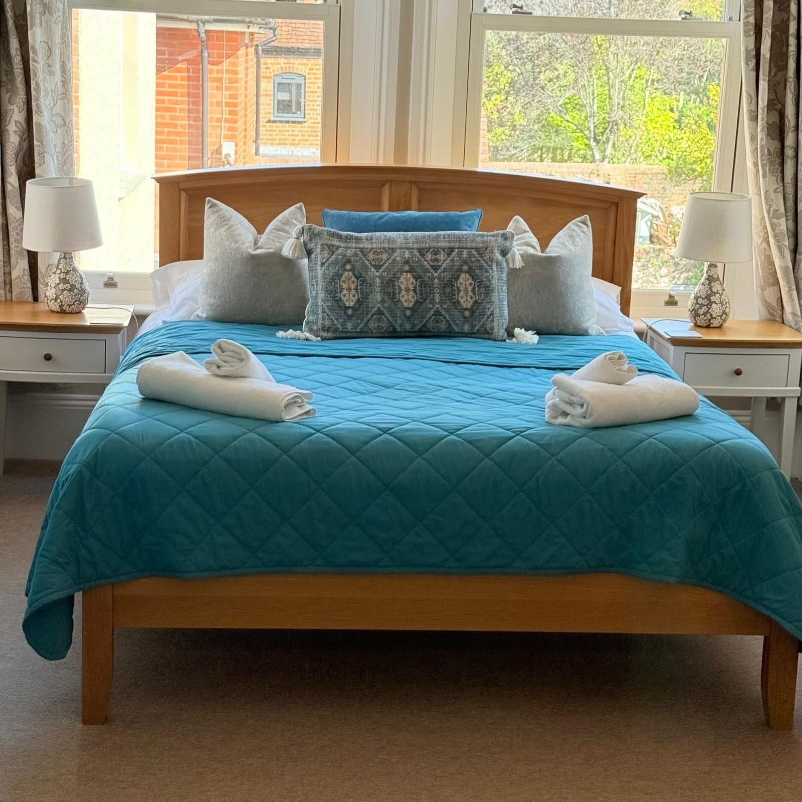 A bed with a blue quilt, two white towels, and multiple pillows.