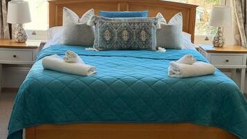A bed with a blue quilt, two white towels, and multiple pillows.