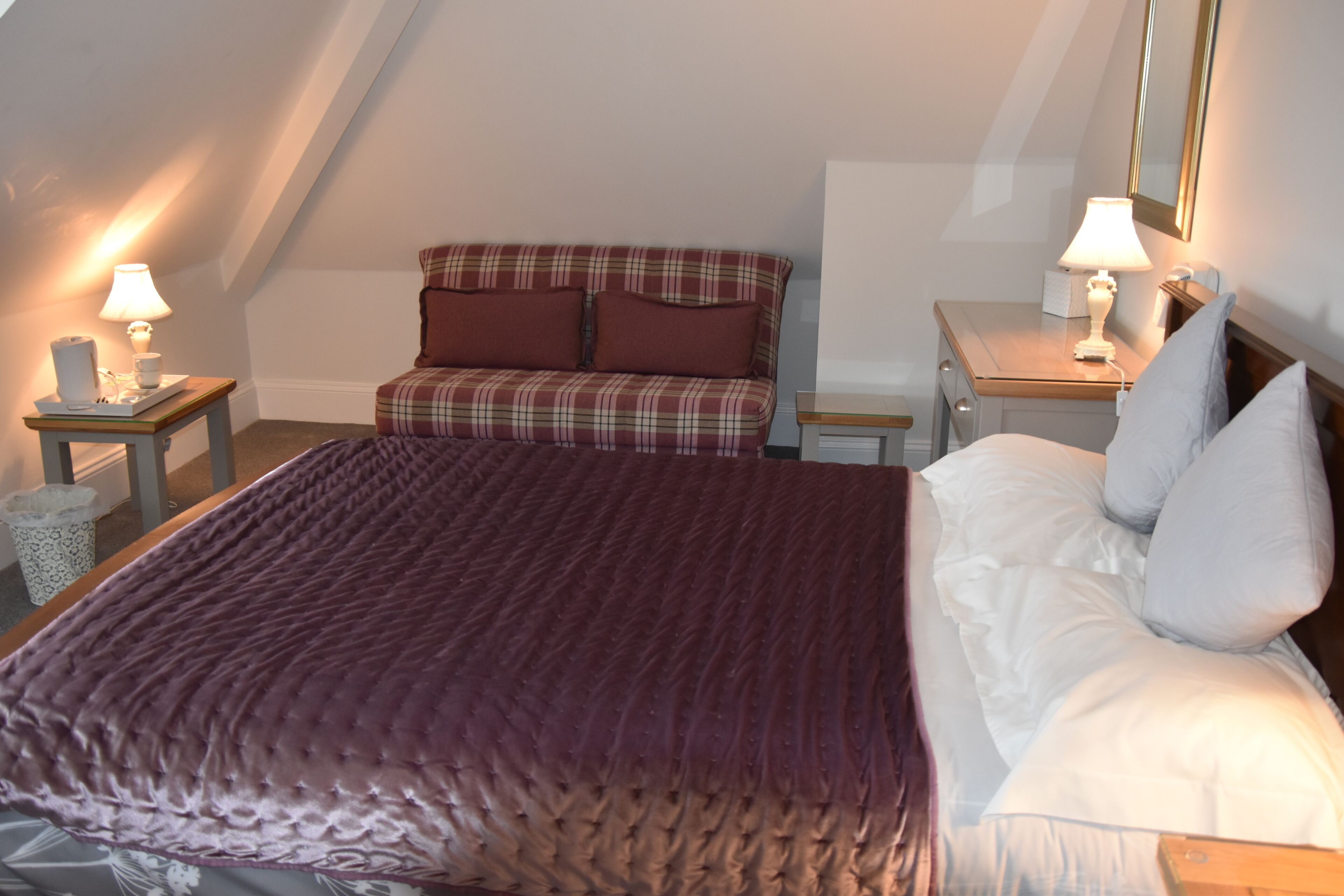 A bedroom with a large bed, a sofa, and two bedside tables with lamps.