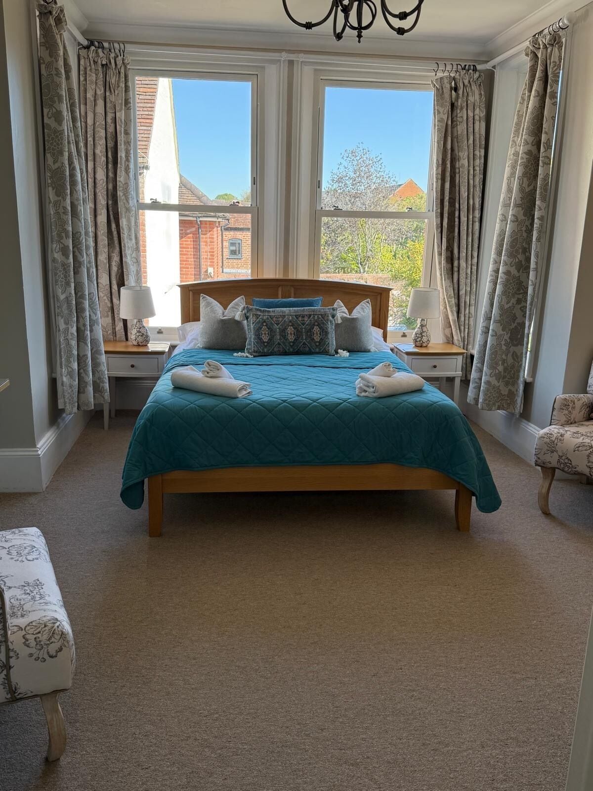 A bedroom with a large bed, two bedside tables, a chair, and a view of a brick building.