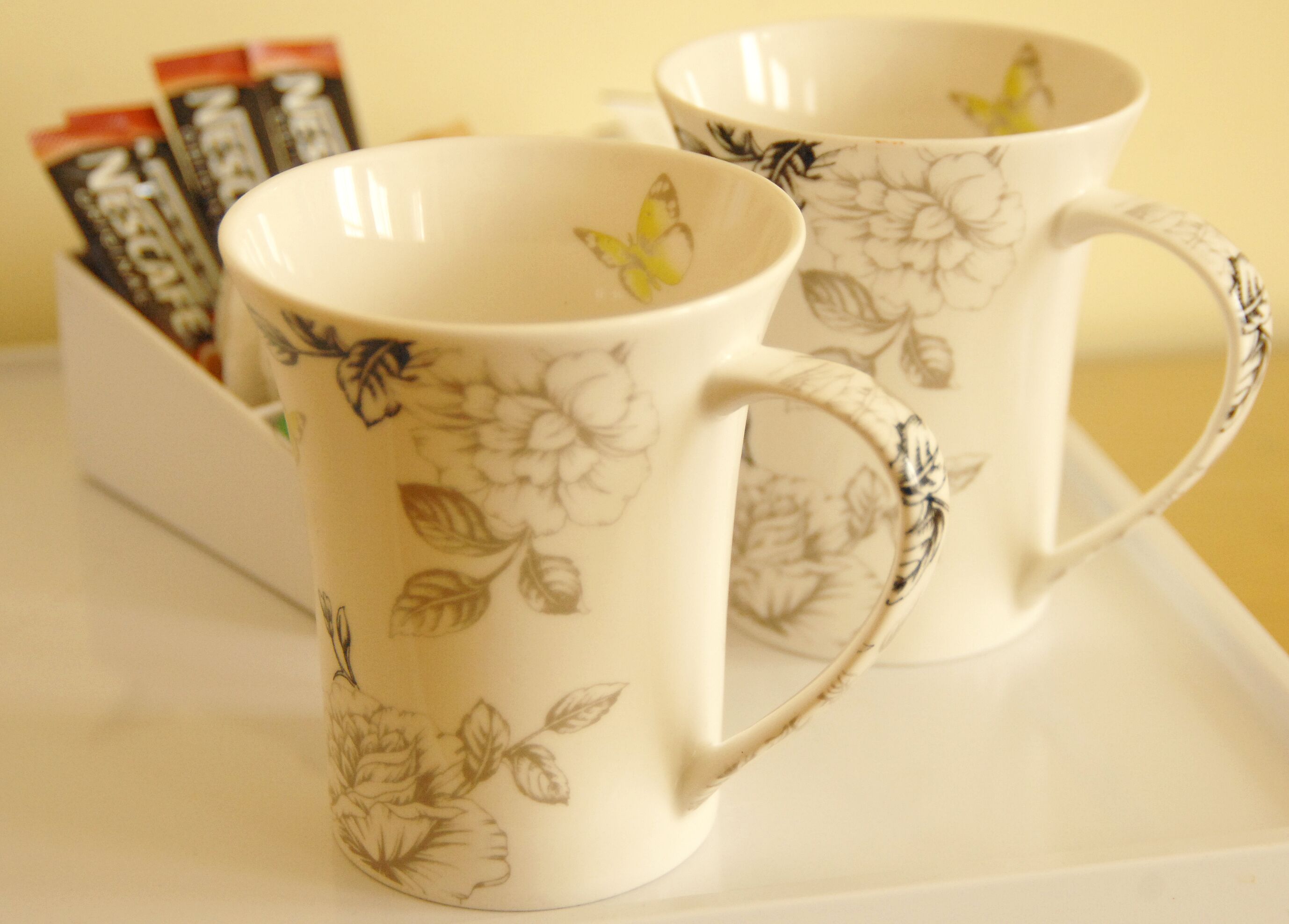 Two white ceramic mugs with floral designs and handles, placed on a white tray.