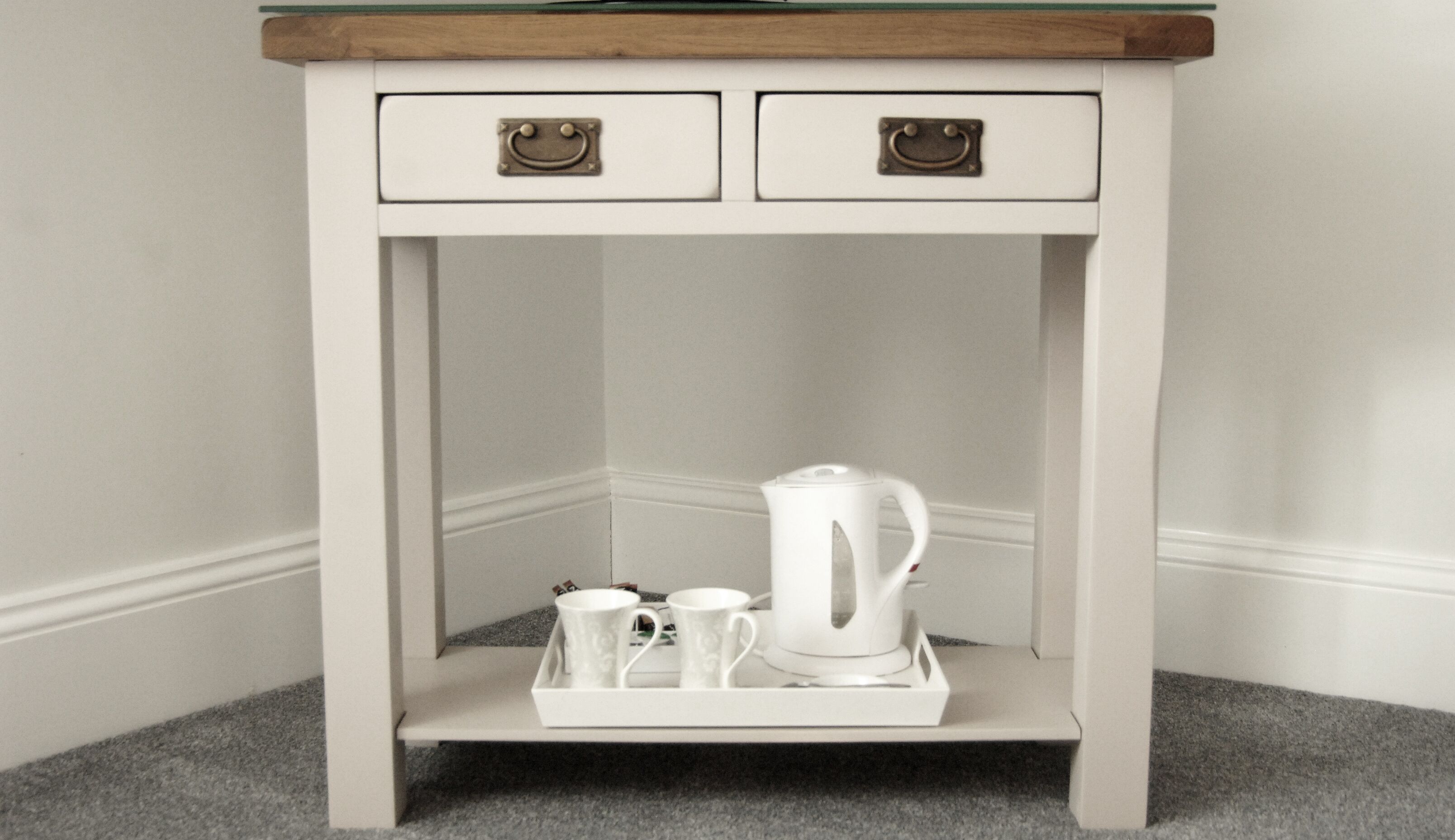 A white table with two drawers and a tray holding a teapot and two cups.