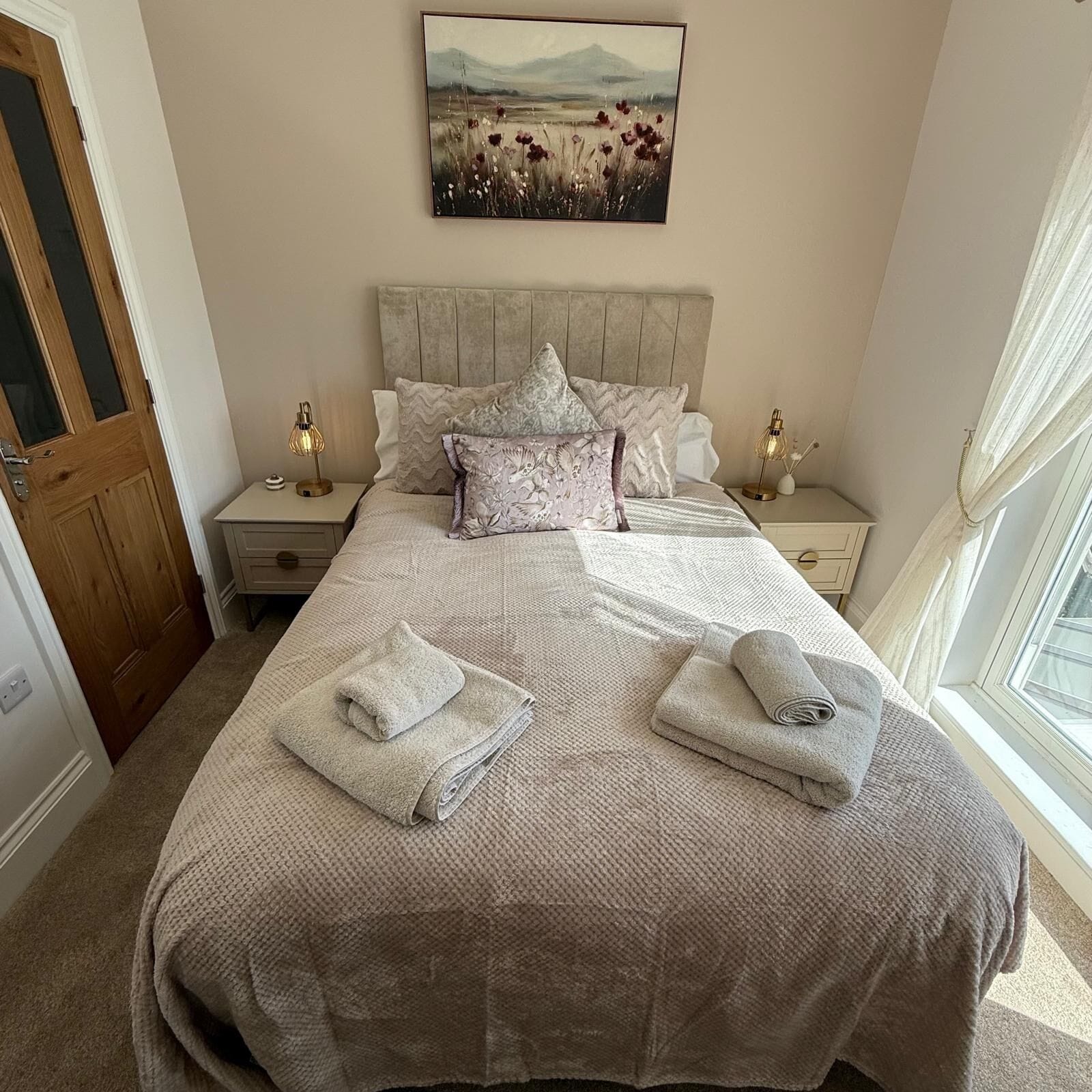 Een slaapkamer met een bed, twee nachtkastjes, een schilderij aan de muur en een raam met gordijnen.