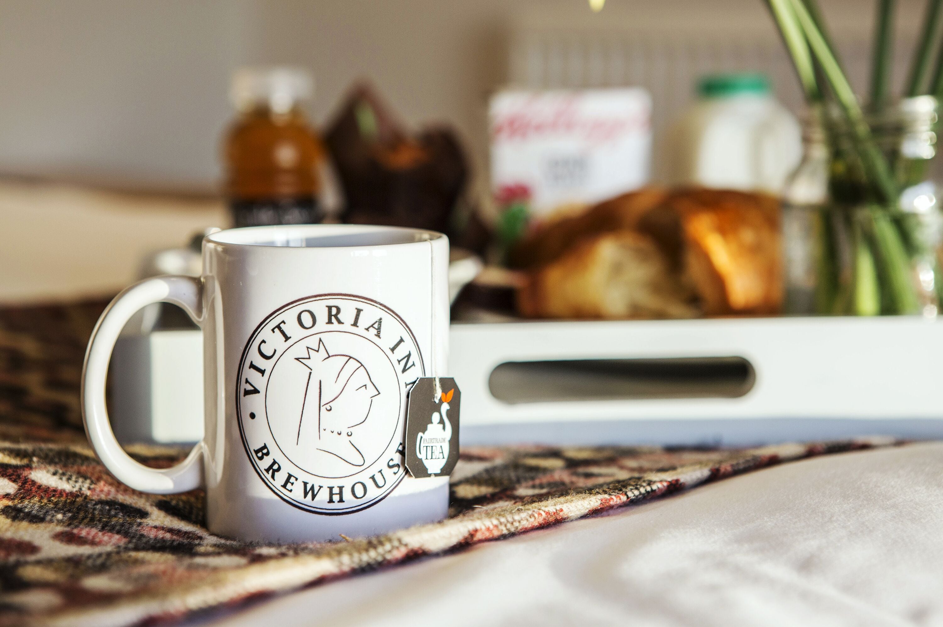 A Victoria In Brewhouse mug on a table with a tray containing bread and condiments.
