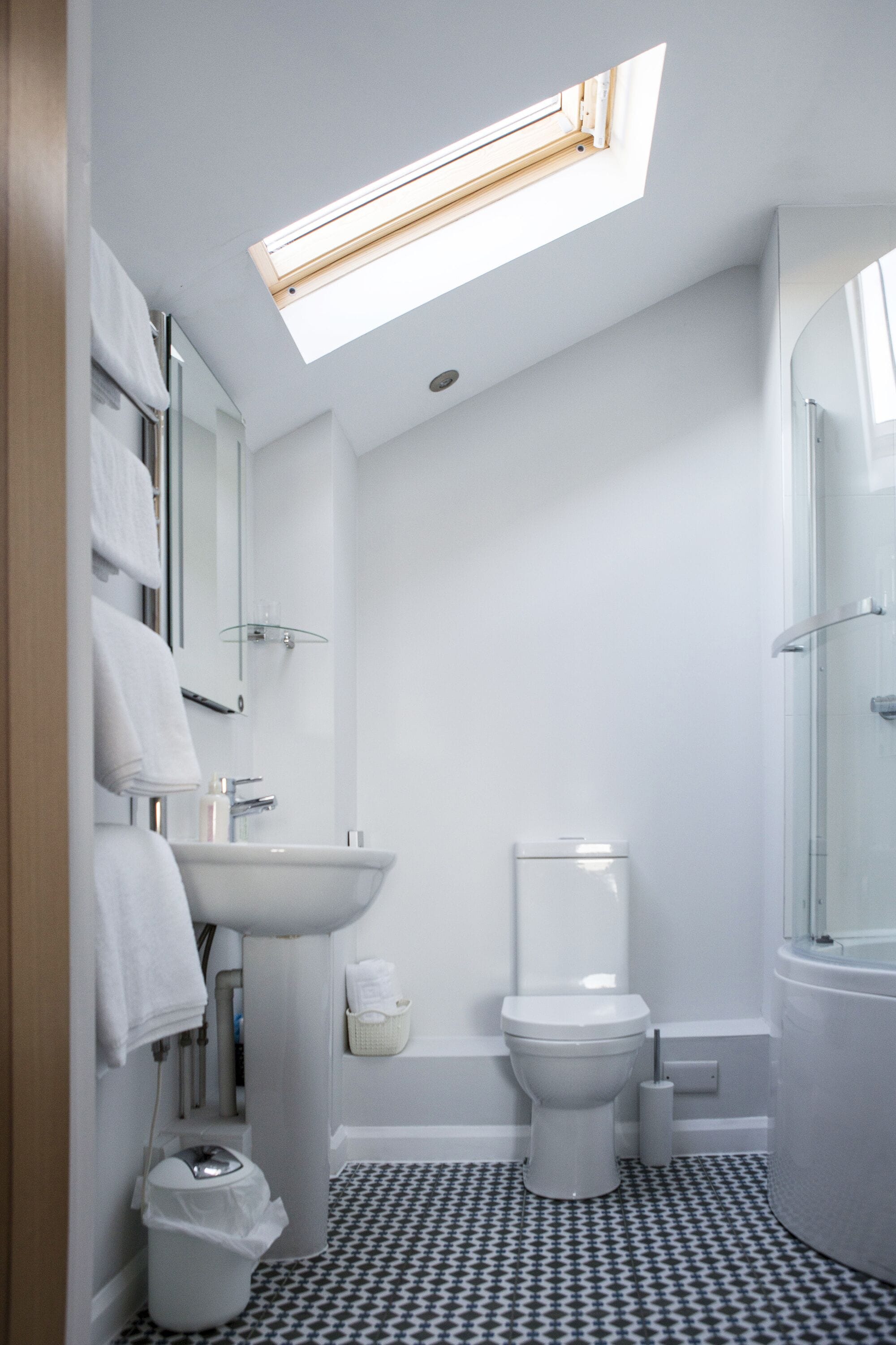 A modern bathroom with a skylight, a white sink, a toilet, and a shower area.