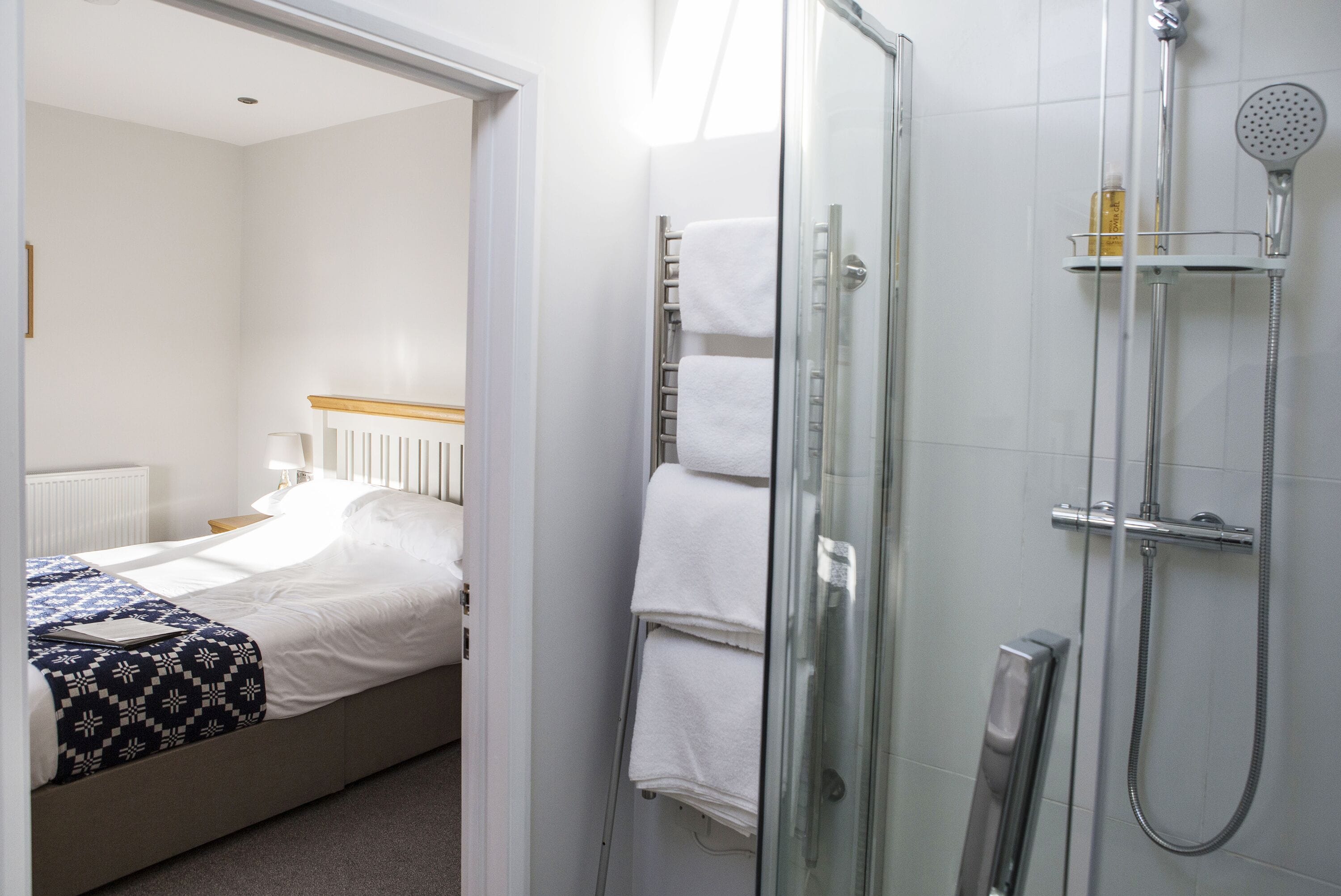 A hotel room with a bed, a glass shower enclosure, and a towel rack.