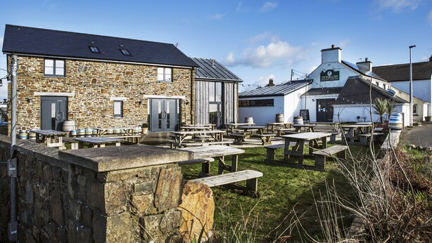 A stone building with a pub sign, outdoor seating, and a grassy area. - Victoria Inn Brewhouse B&B (Haverfordwest)