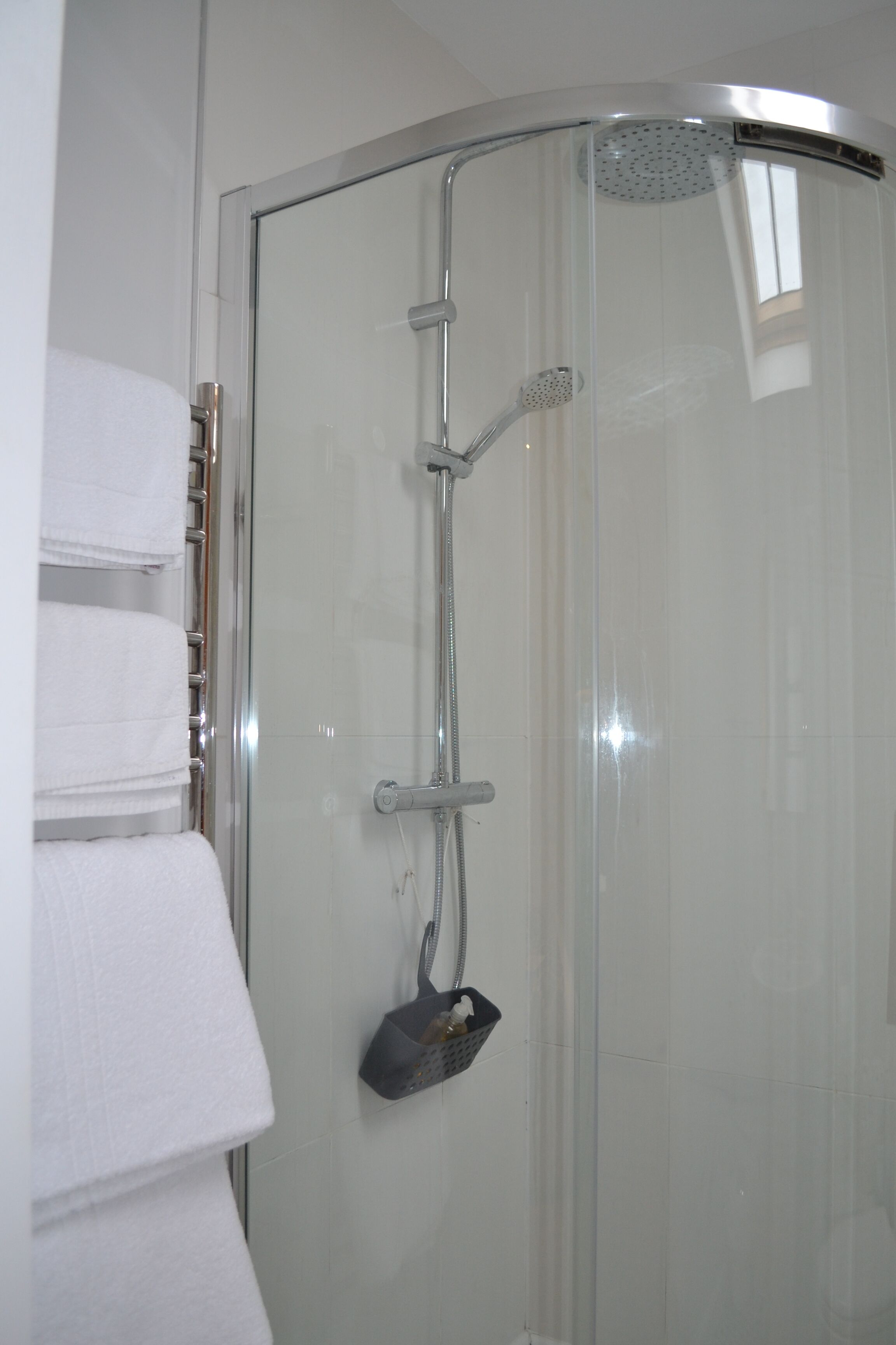 A glass-enclosed shower with a handheld showerhead and a wall-mounted faucet.