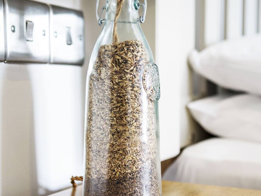 A clear glass bottle filled with seeds, placed on a wooden table with a magazine.