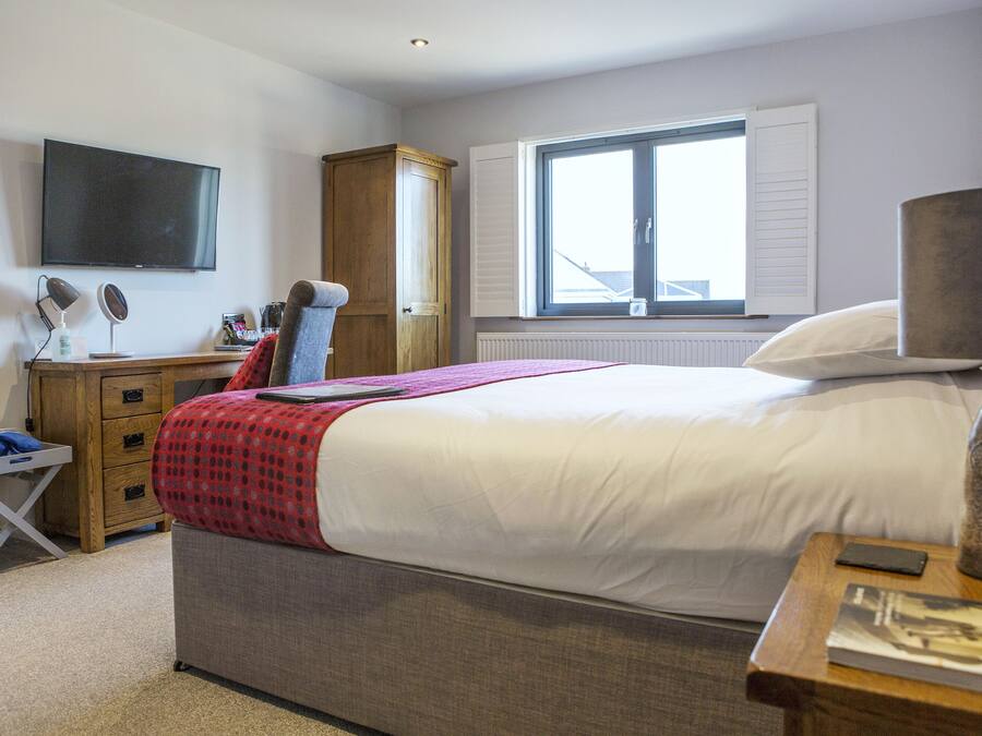 A bedroom with a bed, bedside table, lamp, and a TV mounted on the wall.