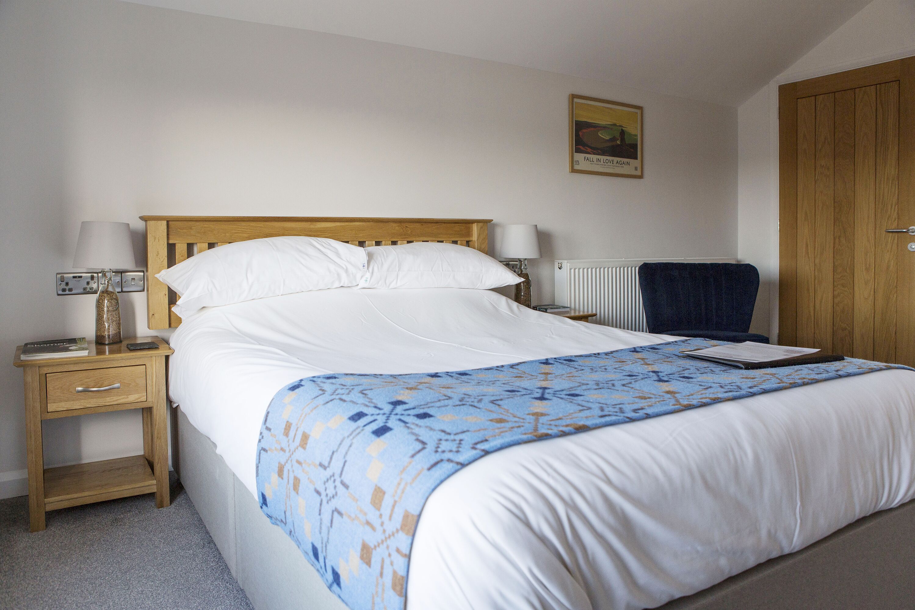 A neatly made bed with a blue patterned bedspread, a wooden headboard, and a white pillow.