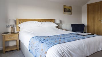 A neatly made bed with a blue patterned bedspread, a wooden headboard, and a white pillow.