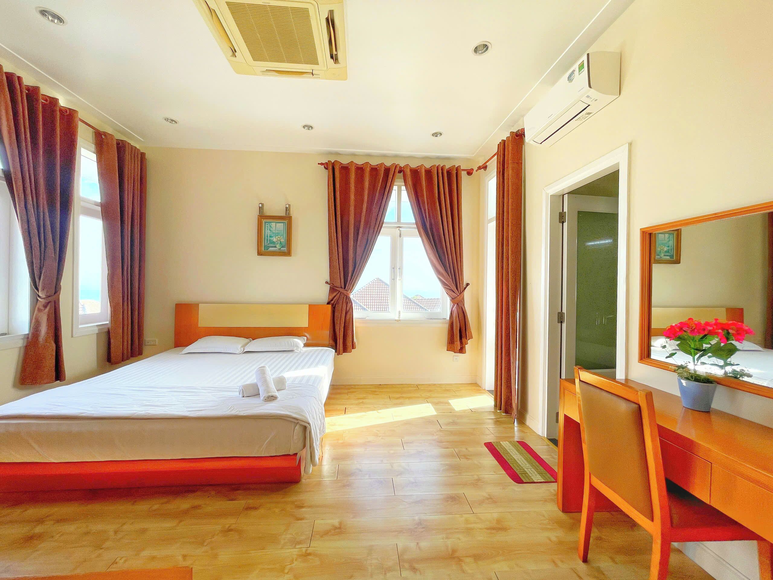A hotel room with a bed, a desk, a chair, a mirror, and a window with curtains.