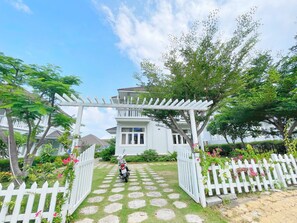 A gated entrance with a white fence, a pathway leading to a building, and lush greenery. - Sealink Villas Phan Thiet Mui Ne (Phan Thiet)
