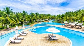A resort pool area with palm trees, lounge chairs, and umbrellas.