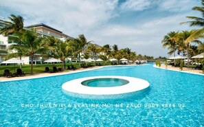 A swimming pool with a circular center, surrounded by palm trees and lounge chairs, with a hotel building in the background. - Sealink Villas Phan Thiet Mui Ne (Phan Thiet)