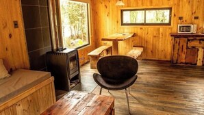 Un interno accogliente di una baita con finiture in legno, un camino in pietra, un tavolo da pranzo e una sedia nera.