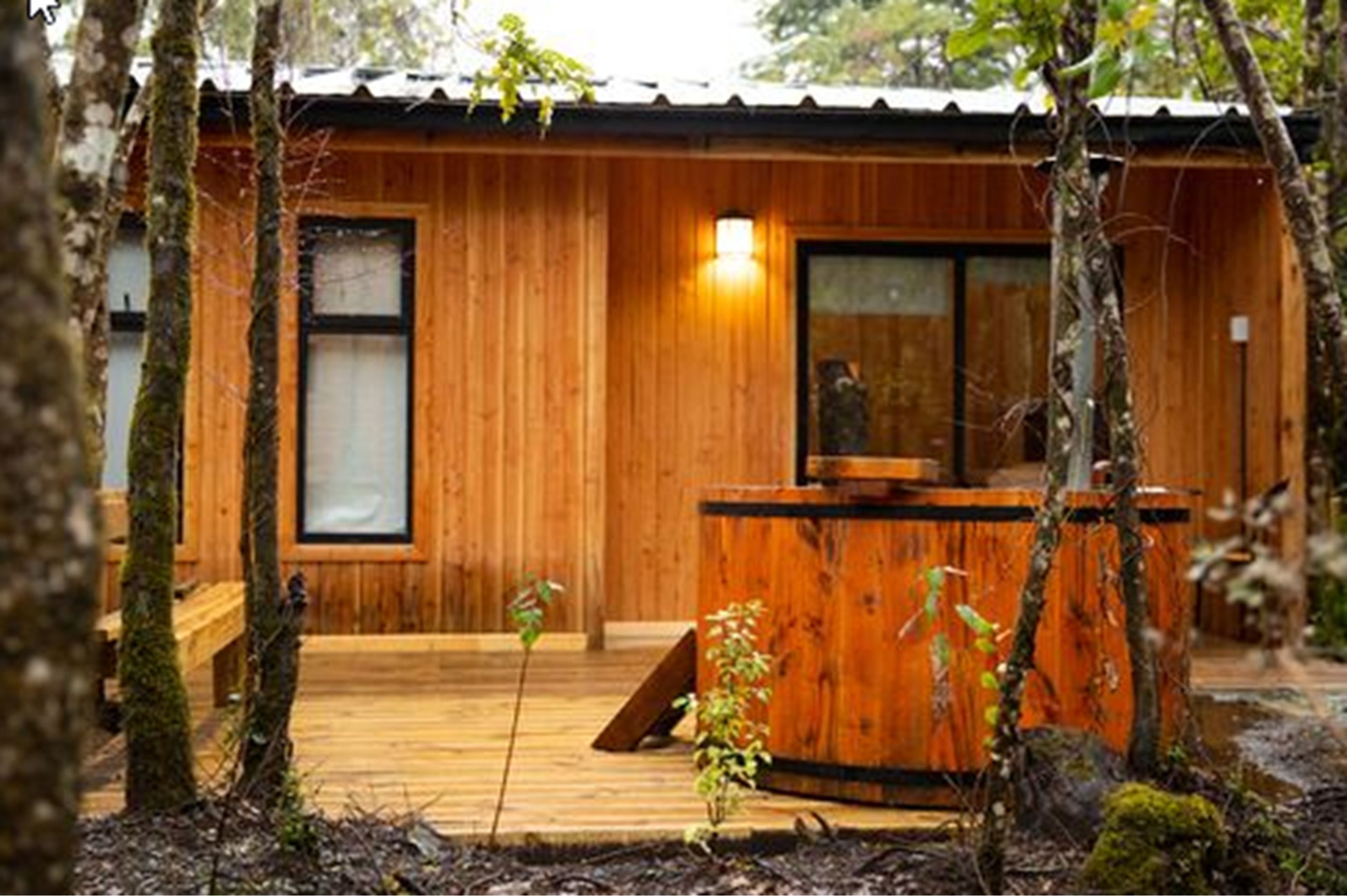 Una cabaña de madera con un balcón de madera, un porche pequeño y una ventana con una lámpara.