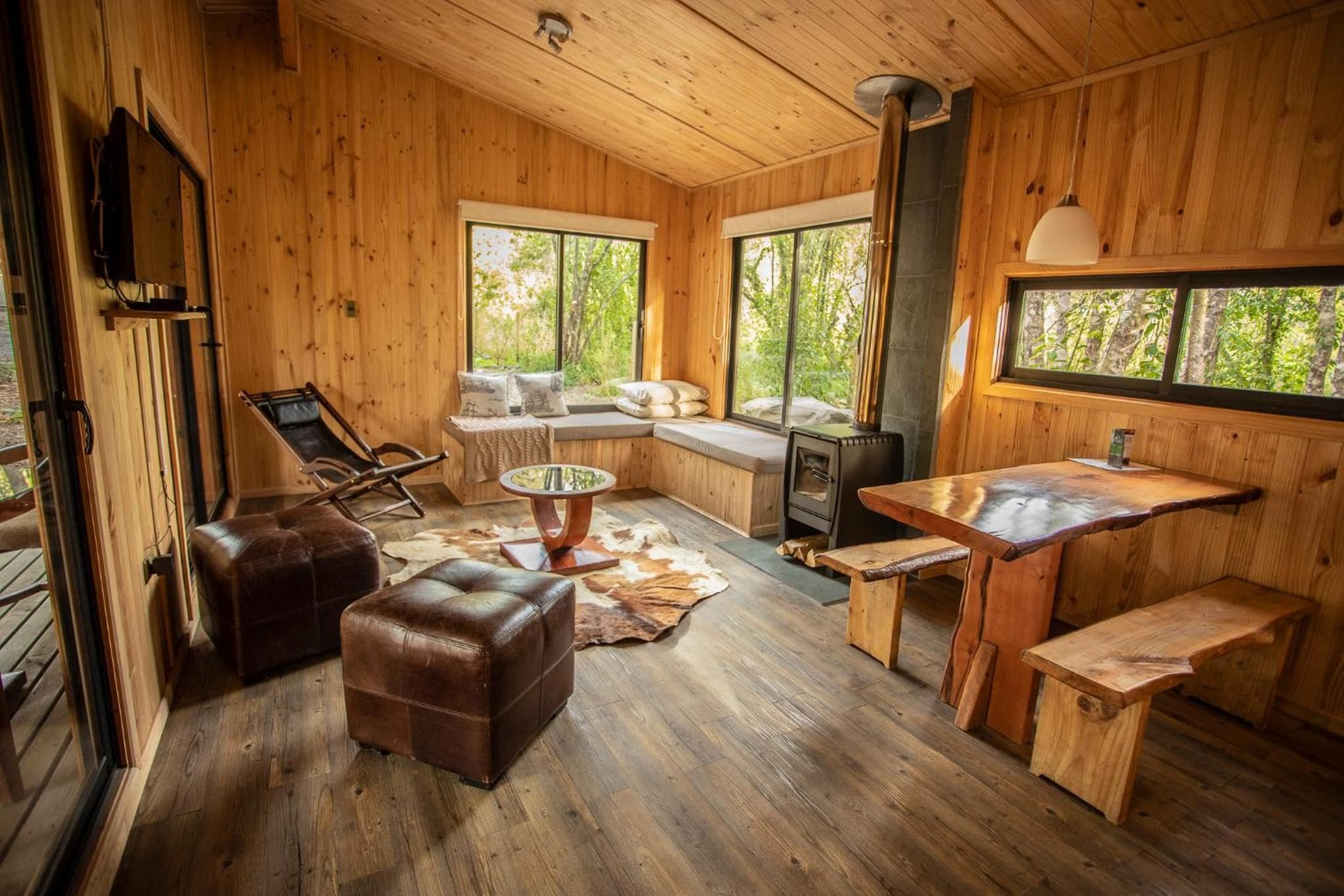 A wooden cabin interior with a sofa, ottoman, dining table, and a fireplace.